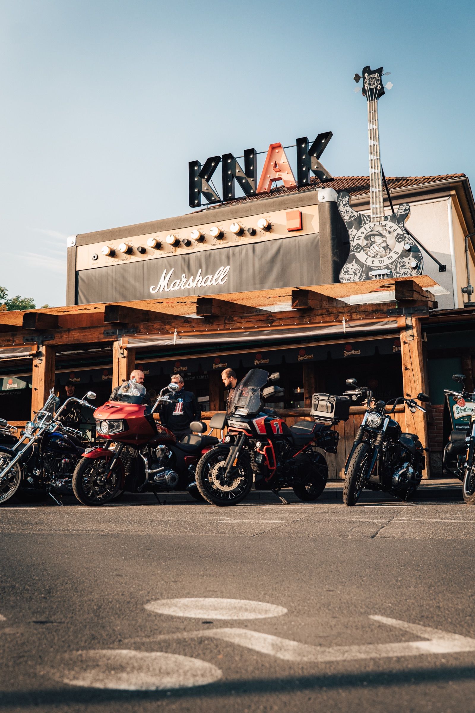 Průčelí KNAKu s kytarou na střeše a motorkami u terasy